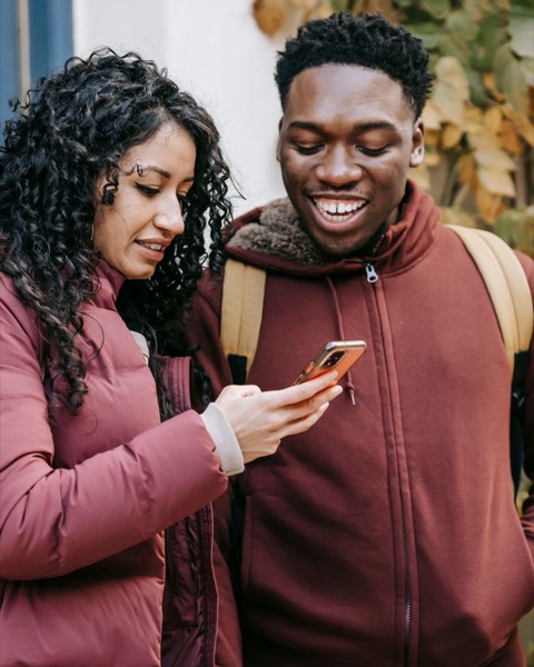 A young couple outside a front door, reading a project on her phone