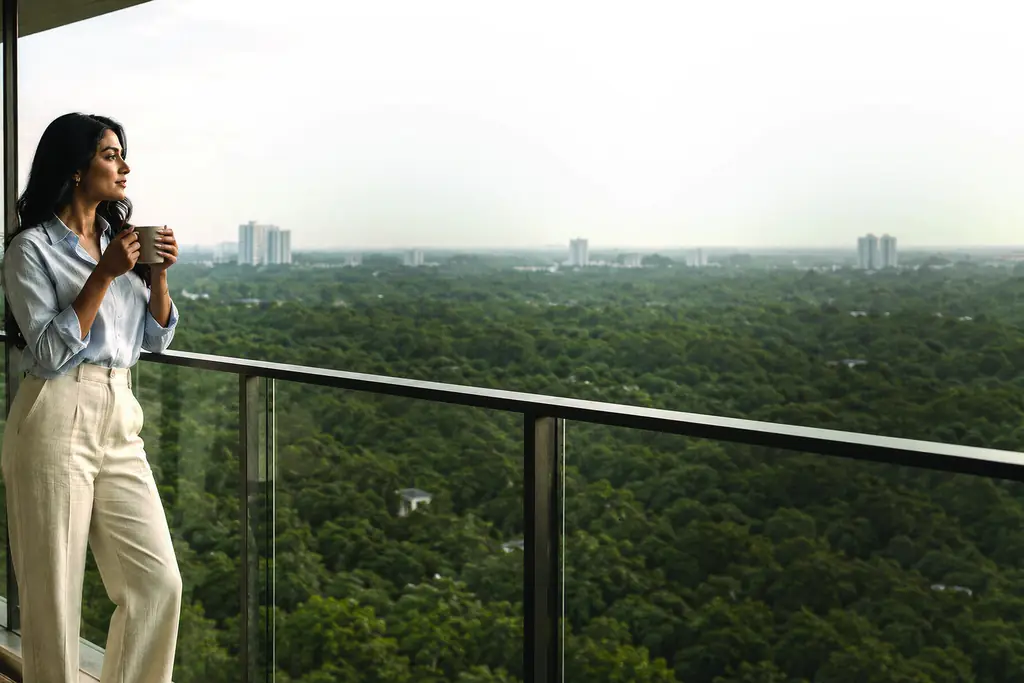 A woman with a cup on a glass-railed balcony above a wide green canopy