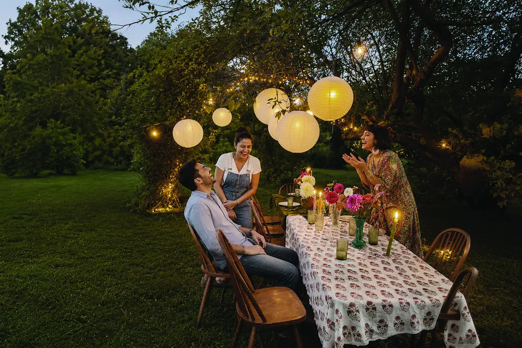 Friends at a long garden table under paper lanterns at dusk