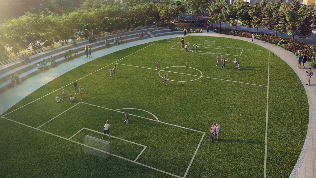 Children playing football on a full-size grass pitch ringed by a running track and trees, a tower at the edge
