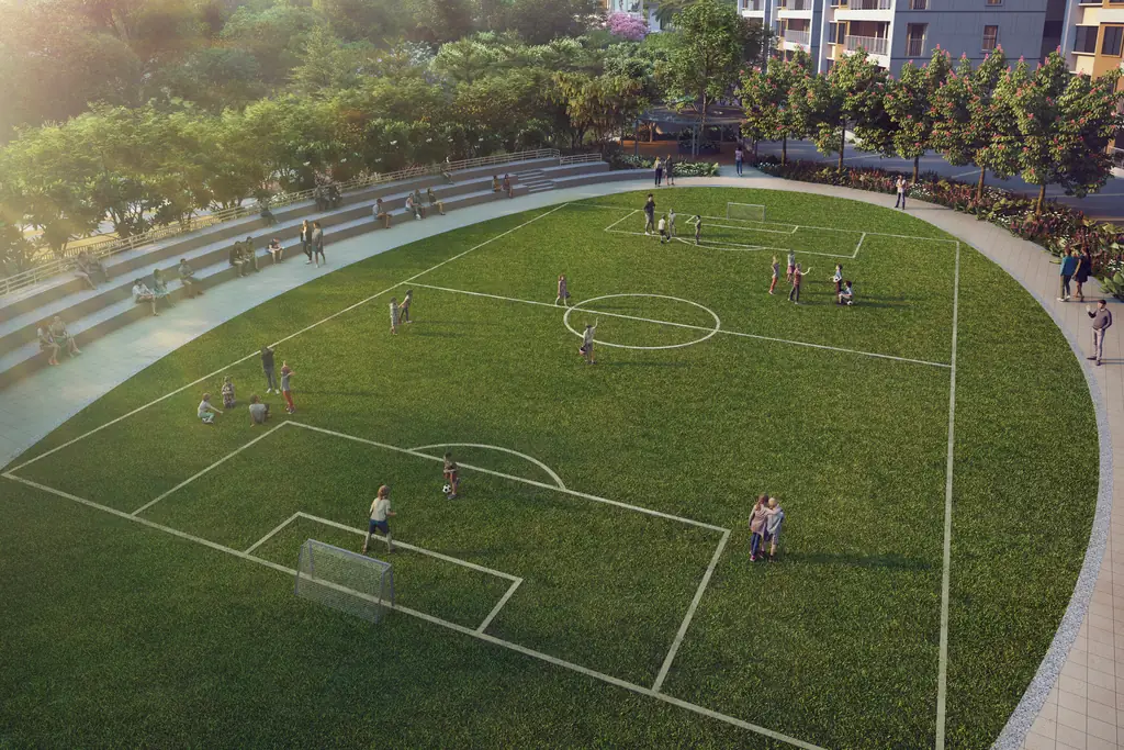 Children playing football on a full-size grass pitch ringed by a running track and trees, a tower at the edge