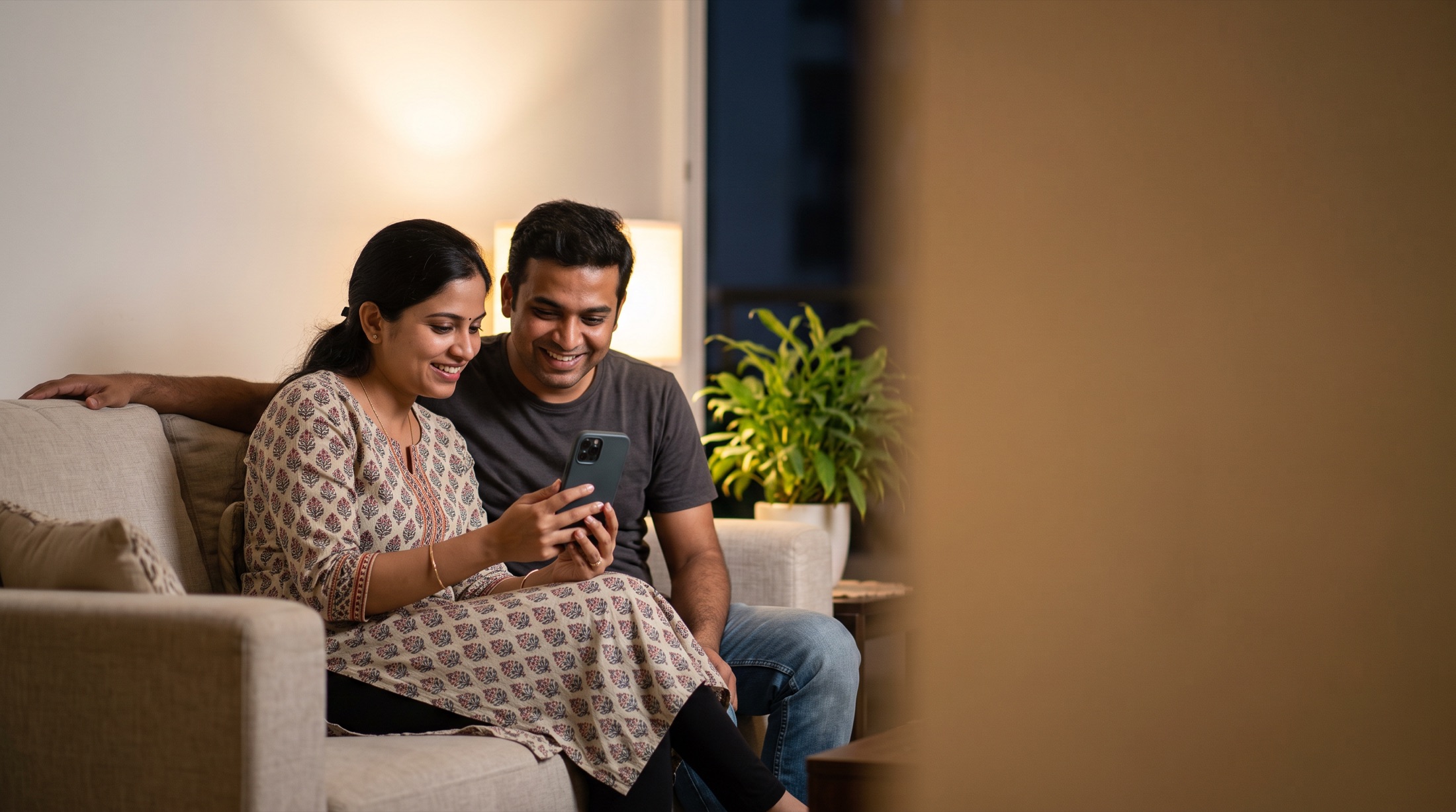 A couple on their sofa late in the evening, smiling at a reply on her phone
