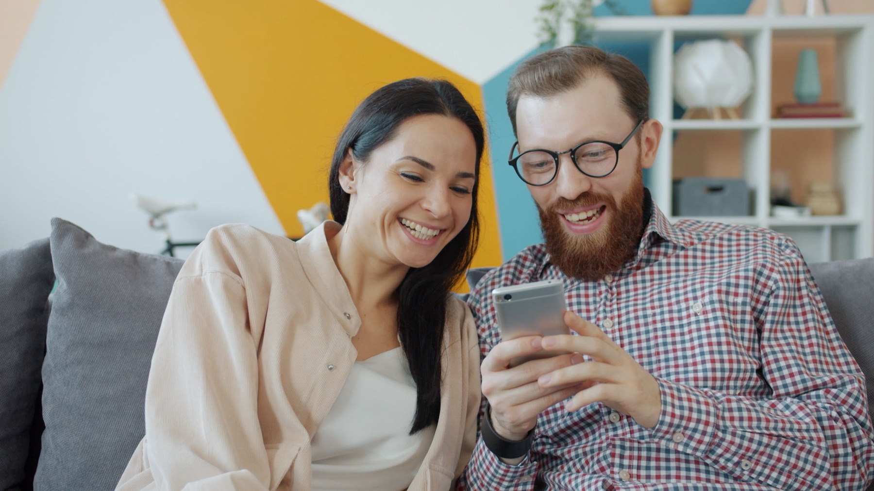 A couple on the sofa, laughing at the project on his phone