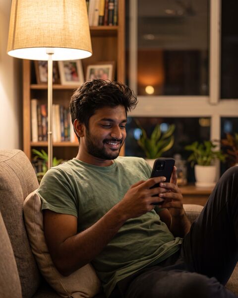 A young man on his sofa late in the evening, smiling at a reply on his phone