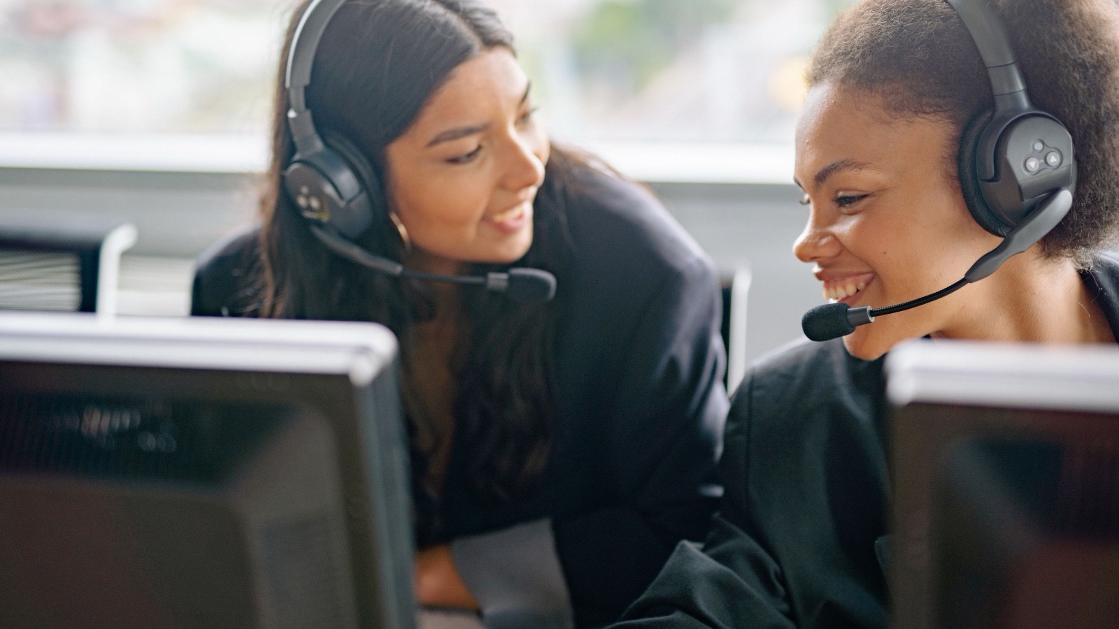 Two agents in headsets at the calling desk, smiling at the screen